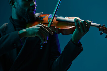 Elegant musician in suit playing the violin under a blue light against a blue background