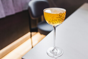 Close-up of a stemmed glass filled with golden-colored liquid, possibly a cocktail, set on a table...