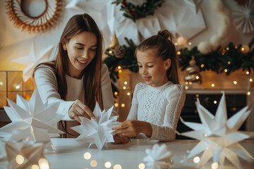 A mother and daughter sitting at a table, creating paper stars in white for Christmas decoration for New Year's Eve, laughing together while making snowflakes of origami from white card stock - Powered by Adobe