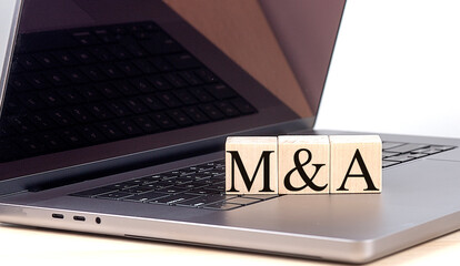 M and A word on wooden block on a laptop , business concept