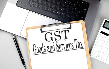 GST -GOODS AND SERVICES TAX word on clipboard on laptop with calculator and pen