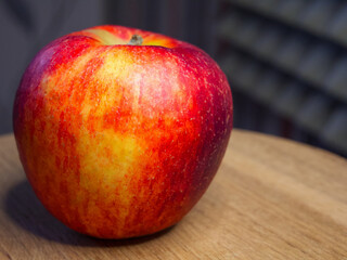 Vibrant red apple, stem intact, water droplets, wooden surface, grey patterned background.