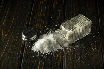 A pile of salt is poured from a hodgepodge on a black table. The concept of excessive salt...