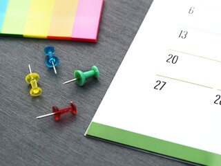 Monthly calendar, unstuck push pins, and colored page markers on a table. Tools for marking events on a schedule and a close-up of a planner. Time management concept