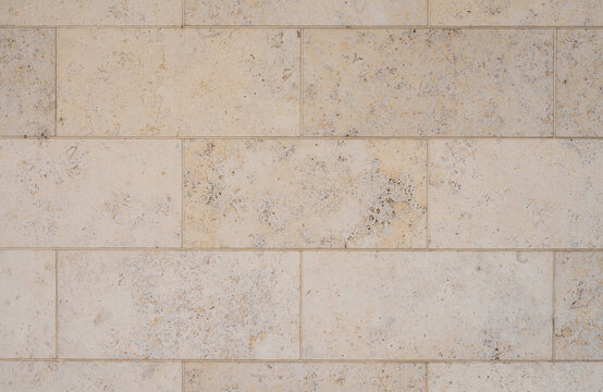 texture of a tiled beige stone wall as background, natural stone wall texture as background. Close-up of a wall clad in limestone