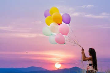 Cheerful cute girl holding balloons running on green meadow violet purple pastel sky happiness....