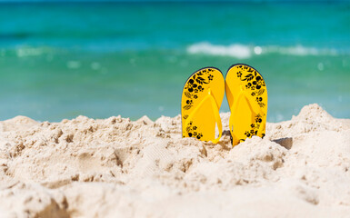 Yellow Sandal rubber shoe on the beach vacation time to travel. Tropical summer beach with sea wave in sunshine day. Slipper shoes outdoor with white wave blue sea on the beach. Summer tropical beach