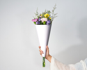 Woman hand holding bouquet of colorful flowers with mockup of blank wrapping paper to add your own...