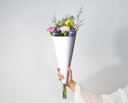 Woman hand holding bouquet of colorful flowers with mockup of blank wrapping paper to add your own information isolated on white background.
