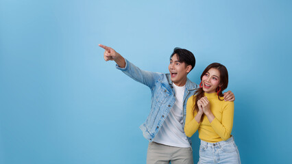 Amazed excited Asian couple tourists pointing hand to empty space isolated on blue banner...