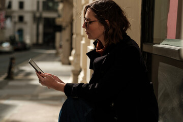 Attractive woman sitting in the street reading an e-reader.