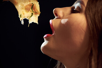Girl with red lips sexy eating a slice of pizza in the evening