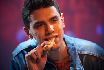 A young guy is eating a piece of pizza in a pizzeria.