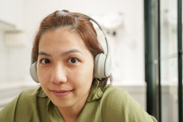 Portrait of beautiful Asian woman smiling while wearing headphones and listening to music, relaxing...