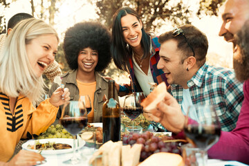 Happy friends having bbq dinner party in garden restaurant - Multiracial young people eating grill meat and drinking red wine in backyard - Food life style concept with guys and girls sitting outdoors