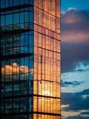 High-rise office building of glass reflecting sunset sky and clouds, urban solitude below.