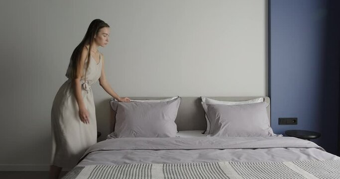 Young woman make bed, set up pillow in bedroom. Interior design of bedroom in blue and grey colors. Modern simple bedroom design