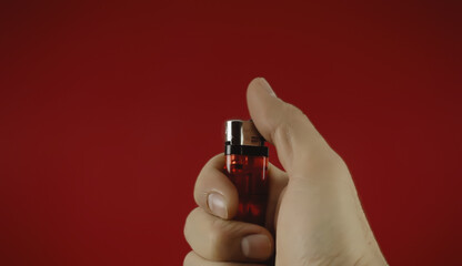 Operating a cigarette lighter (currently off, about to be ignited by a male hand). Colorful closeup shot against a red background.
