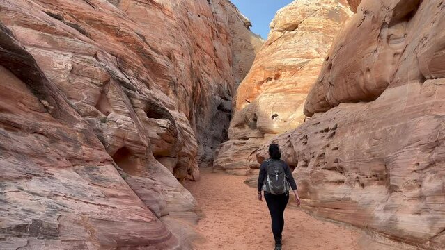 Female hiker walking into the narrow, pink and perfectly carved by erosion walls of the Kaolin Slot Canyon - Valley of Fire State Park, Nevada, USA
