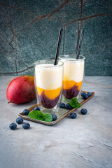 Traditional striped milk shake with mango, blueberries and buttermilk served in a glass as close-up on a design tray