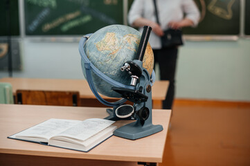 A microscope with a globe is on the school desk