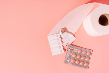 Round tablets and rectal candles in packaging and toilet paper on a pink background.