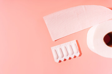 Rectal candles in packaging and toilet paper on a pink background.