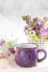 a cup of tea and a branch of lilac on a white background in a basket. Spring Postcard