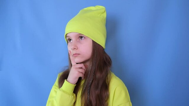 Hmm, let's think about it. Studio portrait of a cute funny little girl thinking about an idea, touching her chin on a blue background.