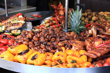 Large round rotating grill with assorted meats and vegetables. Rotary grill. Demonstration of cooked meat, potatoes, mushrooms, zucchini, peppers and tomatoes. Street food. Food court. Fair