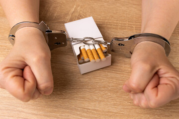 A woman is handcuffed to a pack of cigarettes. Tobacco addiction concept. It's a shame to smoke.