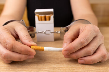 A woman is handcuffed to a pack of cigarettes. Tobacco addiction concept. It's a shame to smoke.