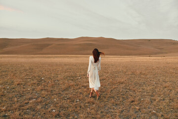 Woman in white dress walking through open field in desert during a scenic adventure trip