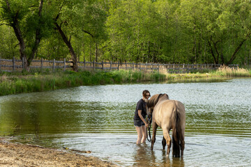 A young woman with her horse stands in a pond.