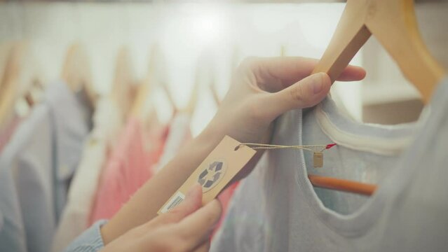 Fashion hangers. In stylish accessories store, young woman in trendy clothes pays attention the clothing reuse signs. He enthusiastically follows fashion trends and holds a tag with a recycling symbol