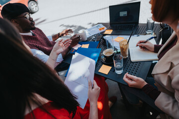 Entrepreneurial team strategizing with documents and laptop at an outdoor setting, reflecting...