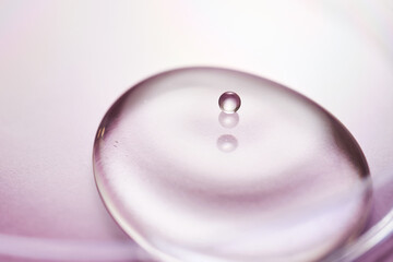 Serum or cosmetic oil flows into a transparent bowl on a purple background.