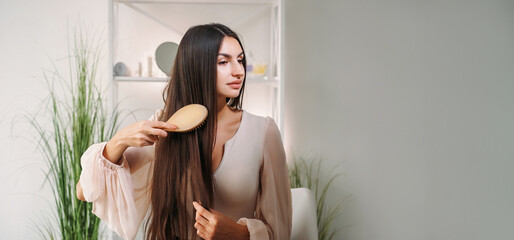 Hairbrush routine. Domestic care. Beautiful young calm elegant woman combing healthy thick straight...