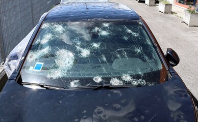 Windshield and body of a car severely damaged by hailstorm. Front view of unrecognizable vehicle..
