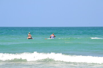 Two women are paddleboarding on the turquoise waters, with waves gently cresting at the shore beneath a clear blue sky at Ponce Inlet, Florida.