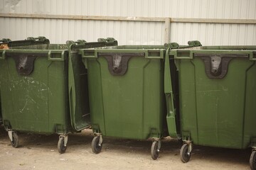 Three green dumpsters standing in a row near a metal fence