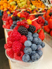 Colourful and healthy fresh berries fruit in plastic bowl at street food market. Spot focus.