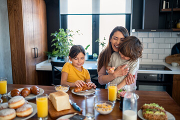 Two happy kids, boy and girl enjoying breakfast with mother. Smiling beautiful mother laughing and...