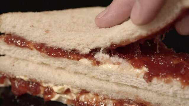 Hand opens breakfast sandwich revealing jam and butter inside.