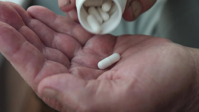 Closeup hands with wrinkled takes out pill from bottle on palm. Chronic disease treatment health care. Takes aspirin antibiotics painkillers. Vitamins and trace elements. Elderly people takes medicine