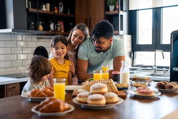 Happy parents spending quality time in the morning during weekend having breakfast with children, small lovely boy and girl in the kitchen.