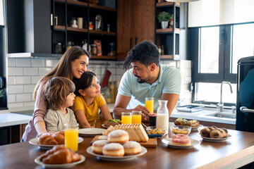 Two cheerful parents talking with their kids during breakfast at home.