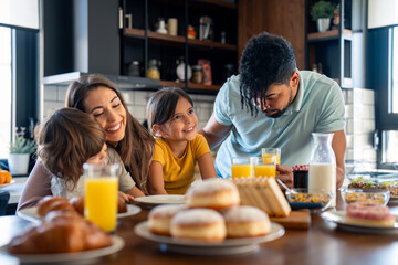 Cheerful couple bonding and embracing with children during breakfast time at kitchen table at home.