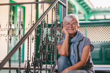 Portrait of attractive elderly woman white haired sitting on a staircase looking at camera smiling