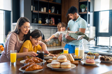 Young girl with her mom preparing breakfast while dad is playing with son in the background.